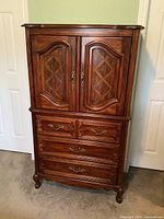 Front view of the wardrobe style wood dresser showing four drawers and two door upper cupboard with decorative panels and brass handles.