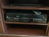 Front view of Toshiba SD-V395 DVD VCR combo unit showing disc tray, tape deck, control buttons, and ports.