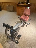Recumbent exercise bike viewed from rear left angle showing padded seat, backrest, pedals, and handlebar grips