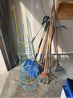 Full view of the garden tools including tomato cages, hoes, rakes, shovels inside a garage.