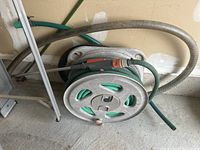 Garden hose coiled on reel beside a wall, showing hose and reel