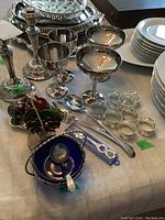 Photo showing the main assortment of metal cups, goblets, candle sticks, and spoons arranged on a table with white cloth.