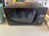 Front-right angle view of black Danby microwave oven on a countertop showing door with window and keypad controls on right side.