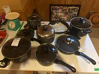 Photo showing various pots and pans including a large covered pot, skillet, and saucepans with glass lids on a table.