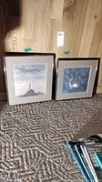 Two framed prints named Archer and Looking Glass leaning against wood panel floor wall, on a textured carpet