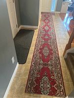 Red polyester runner placed on tiled floor, shows length and design pattern clearly alongside a dark gray door mat.