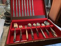 Open wooden chest with red felt interior containing handle ends of forks and spoons arranged neatly