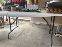 Side view of the shop table showing folding metal legs and plywood top, set in a garage environment.