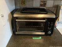 Front view of Hamilton Beach toaster oven showing the racks inside and control panel on the right side, along with measurement tag.