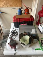 Photo showing red and blue metal oil cans, red Craftsman toolbox, small metal vise, plastic funnel, and sanding drum kit in gray case
