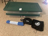 Two Rubbermaid storage totes with green lids, a blue textured tub mat, and two black travel bags shown on beige carpet.
