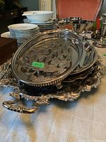 Photo showing stacked metal trays including ornate large tray with detailed engravings and smaller oval tray with openwork sides on a table