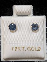 Pair of round blue sapphire stud earrings set in 10K gold displayed on white textured card marked '10KT. GOLD'.