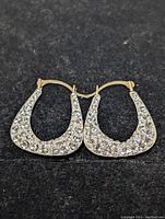 Top view of pair of 10K yellow gold hoop earrings set with clear cubic zirconia stones on black surface