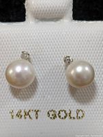 Front view of the earrings showing round white freshwater pearls with 14K gold posts and small diamond accent.
