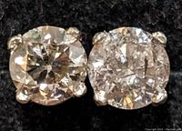 Close-up of two round-cut diamond studs in four-prong 14K gold settings on black background