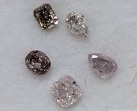 Close-up of five assorted pink diamonds on white background showing color and shape detail.