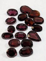 Close-up of 15 garnet gemstones showing varying oval and pear shapes and faceted cuts exhibiting deep red color.