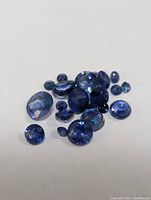 Multiple loose blue sapphires arranged on a plain white background showing various gemstone shapes and rich blue color tones.