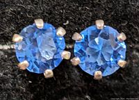 Close-up front view of two silver earrings with round blue gemstones on a black background.