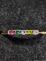 Close-up top view of the silver ring showing five round multicolored stones in a row set on the band.