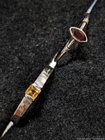 Close-up of two rings, one with a marquise garnet and the other with a square citrine stone, shown on a black textured surface.