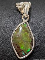 Close-up front view of sterling silver pendant with green iridescent ammolite gemstone on black textured background