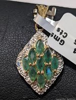 Front view of sterling silver pendant with emeralds and white stones on black background showing the details and stones.