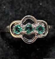 Close-up image of the sterling silver ring showing the three bright green round emerald stones set horizontally with small clear accent stones and openwork detailing on the band.