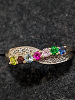 Front view of the sterling silver ring with a row of seven multi-colored round gemstones and small clear stones on each side set into the band.