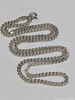 Full length view of sterling silver chain necklace laid out on white background.