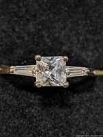 Close-up front view of sterling silver CZ ring showing the princess-cut cubic zirconia center stone and tapered baguette side stones.