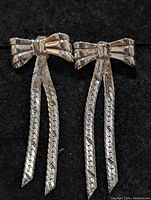 Front view of the pair of sterling silver bow earrings with two braided dangles each on black background.