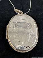 Close-up front view of sterling silver oval locket pendant showing floral engraving.