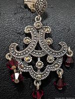 Close-up front view of sterling silver pendant with marcasite stones and hanging red beads on black background.