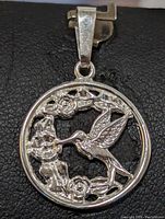 Close-up image of the sterling silver pendant showing the hummingbird and rose design on a black background.