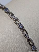 Close-up photo of the sterling silver bracelet showing the polished metal, decorative openwork links, and prong-set tanzanite stones.