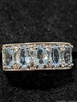 Close-up image of the front side of the ring showing seven oval blue topaz stones set in a row in sterling silver.