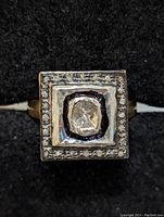 Top view of square ring head showing central round diamond, black enamel border and halo of accent diamonds
