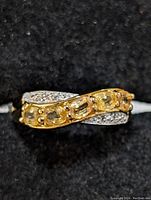 Close-up of the sterling silver ring with yellow sapphire stones on a black fabric background showing the top view with the yellow sapphires and small clear stones.