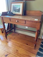 Front and slightly angled view of antique pine writing desk showing central drawer, side and back rails, turned legs, and wear on wood surface.