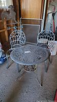 Photo showing full iron bistro set with two chairs and one round table in a garage setting with peeling paint.