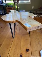 Side view of the unique shaped burl wood coffee table with metal legs on wooden floor.