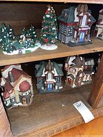 Shelf showing four village houses with snow-covered roofs and a decorated Christmas tree