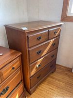 Front angled view showing the 4-drawer wood highboy dresser with metal handles and medium brown finish.