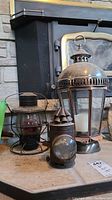 Photo showing all three lanterns in a row on a stone hearth next to a black stove, including the large candleholder lantern, the CNR railroad lantern, and the police signal lantern.