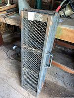 Pair of black metal ramps shown folded and standing upright, with visible wear and rust on the frame and mesh surfaces. Handles visible on the side for managing the ramps.