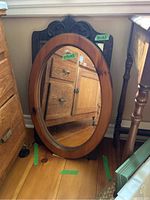 Oval mirror with carved wood backing resting against wall, showing full oval shape and wood details
