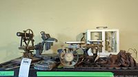 Multiple items on black grid shelving: theodolite, microscope, thermo-hydrograph, scale, weights, anemometer cups