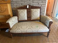 Full view of wooden settee showing floral patterned beige upholstery on seat, back and armrests, with carved wood trim along the edges and legs.